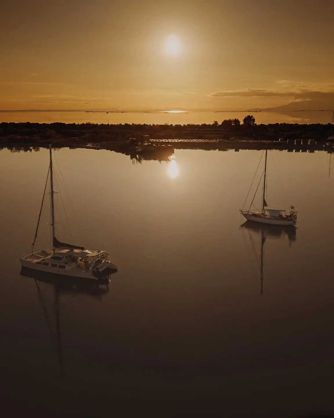 Aerial sunset photograph of a catamaran and sailboat by Dimitris Kyriakoulis