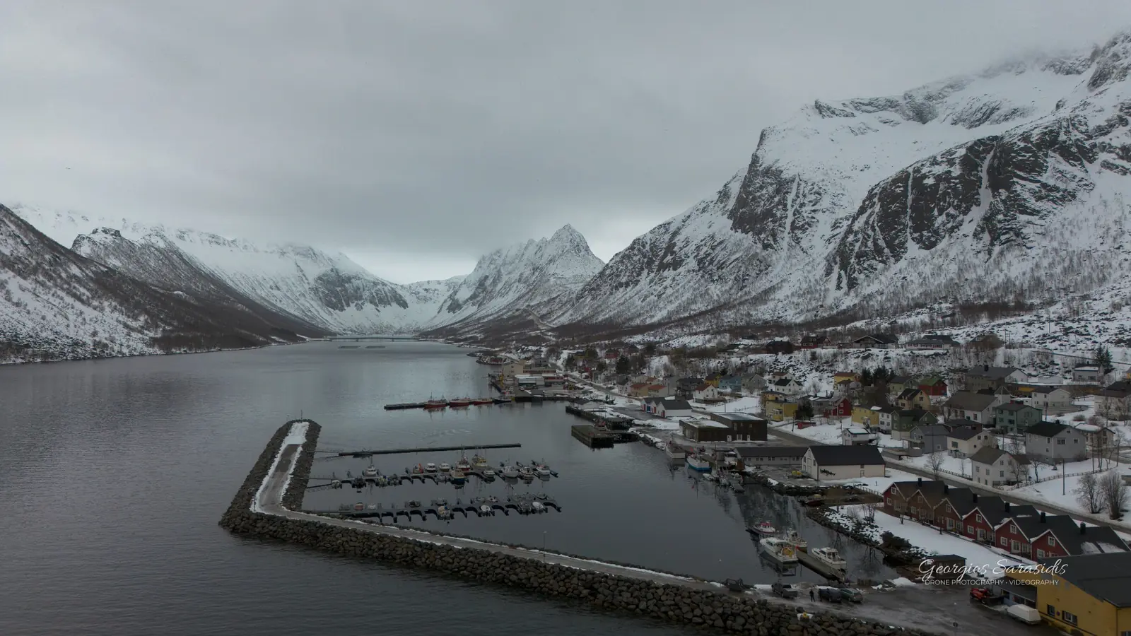 Winter aerial panorama of a snow-covered coastal village and mountain landscape by Giorgos Sarasidis