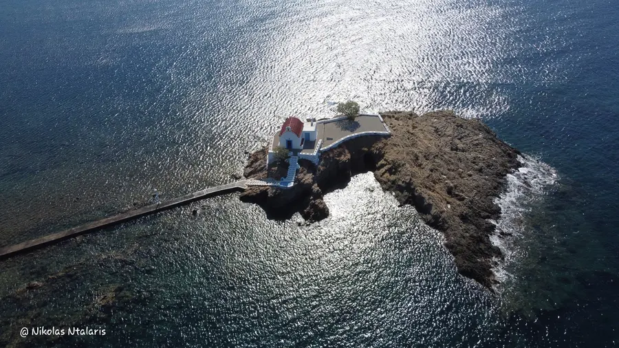 Aerial photograph of a small white chapel on a rocky islet by Nikolas Ntalaris