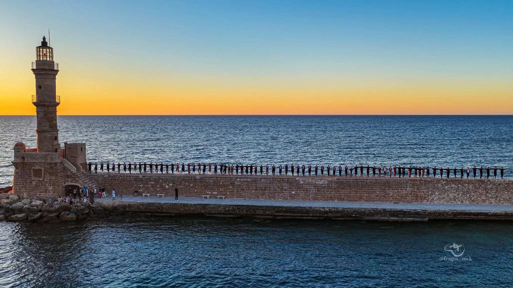 Aerial photograph of a public gathering along the Chania lighthouse breakwater by Nikos Fragos