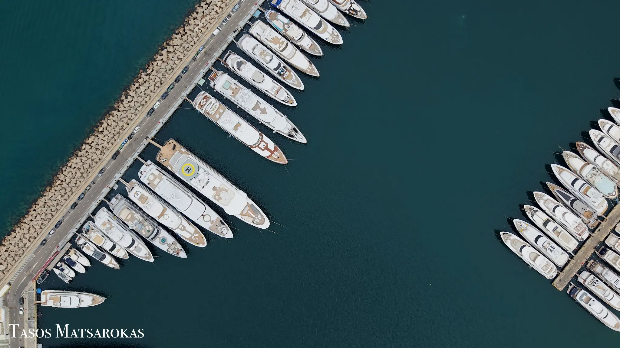 Top-down aerial photograph of yachts along a marina pier by Tasos Matsarokas