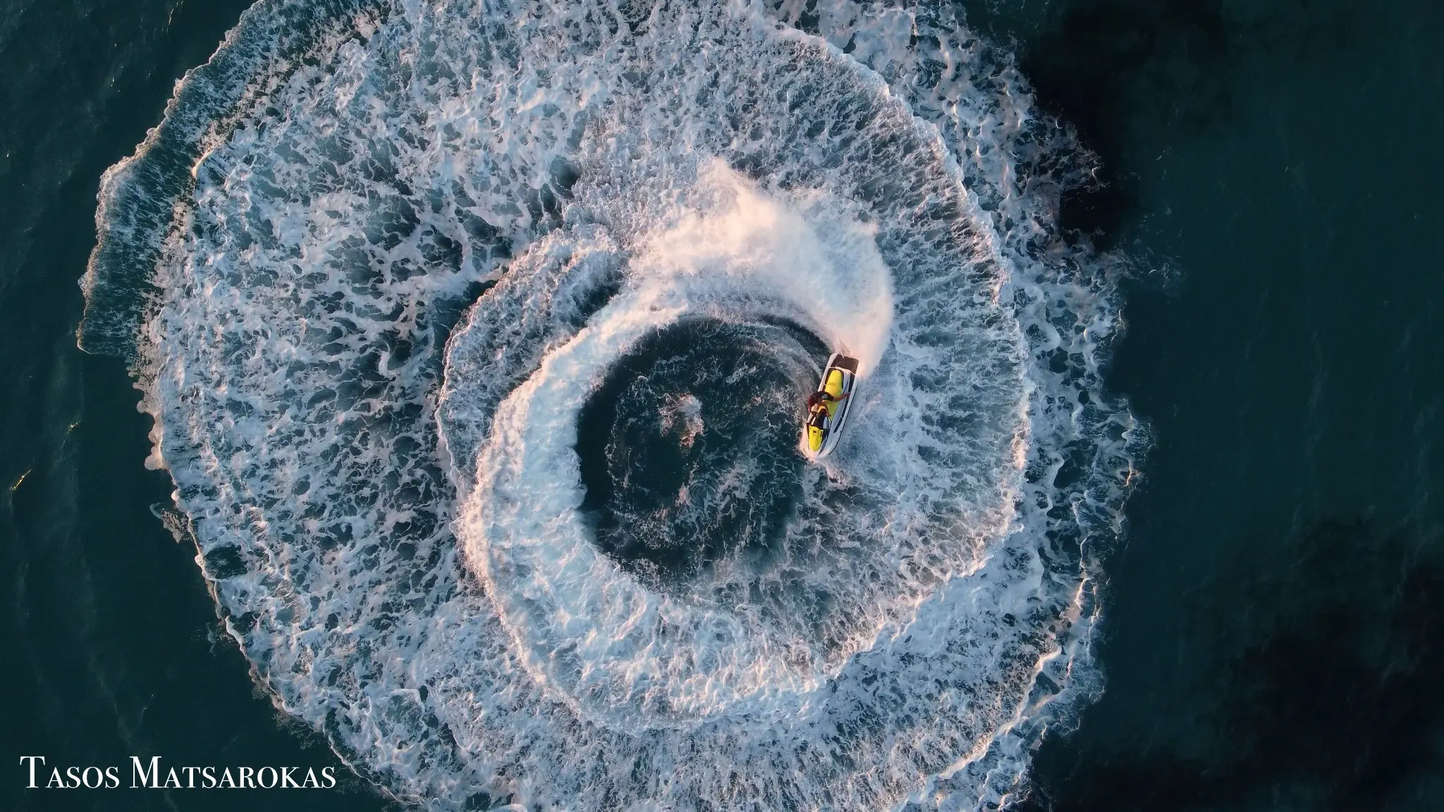 Top-down aerial action photograph of a jet ski carving a circular wake by Tasos Matsarokas