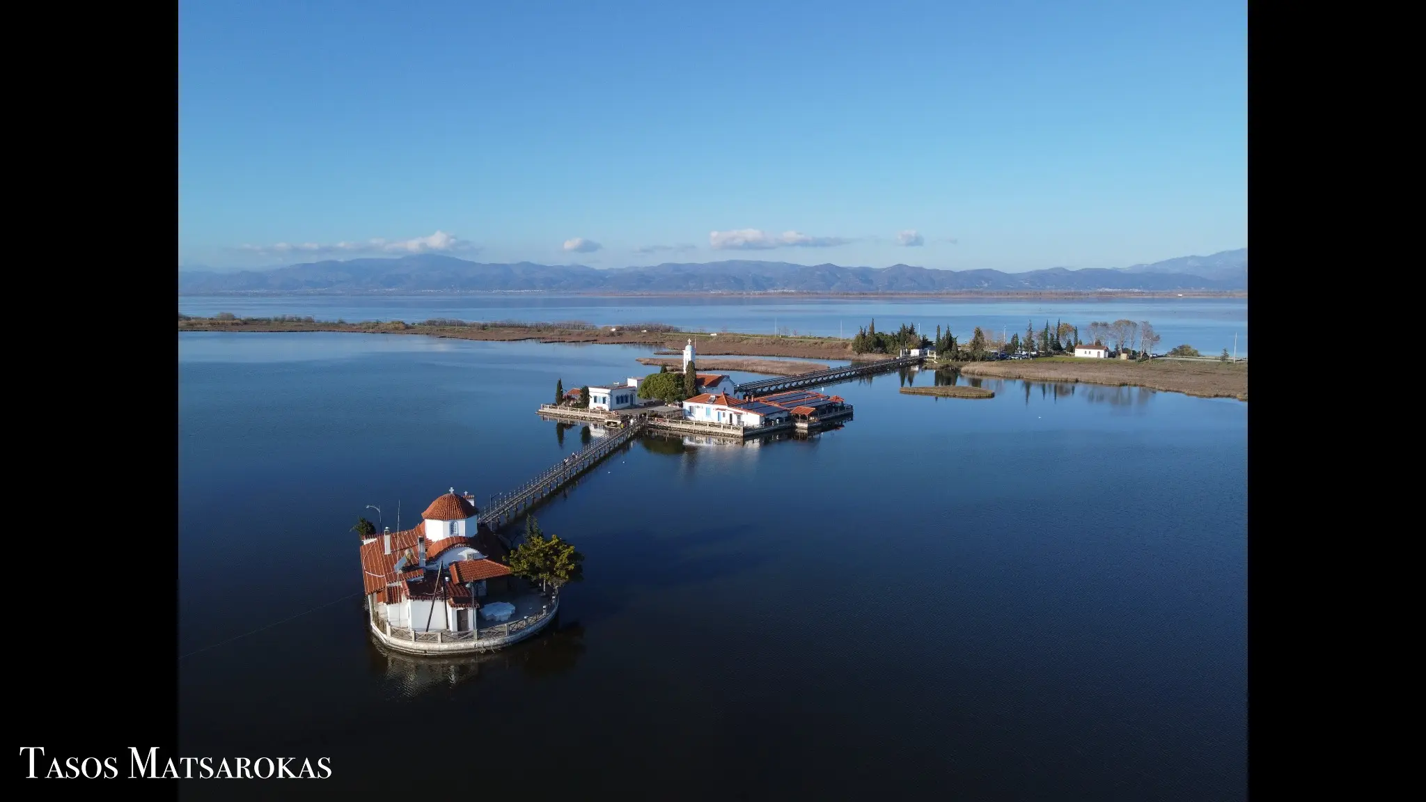 Aerial photograph of a monastery complex surrounded by calm water and nature by Tasos Matsarokas