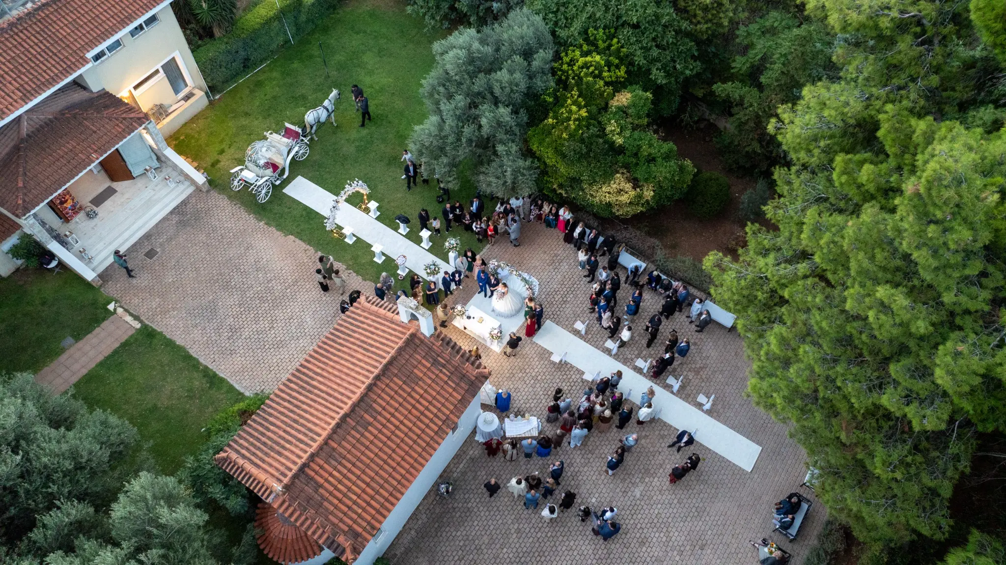 Aerial photograph of an outdoor wedding ceremony with a horse-drawn carriage by Themistoklis Karantinos